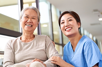 A smiling nurse seated next to an old smiling women and holding her arms